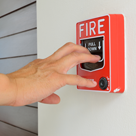 A hand reaching for a fire alarm.