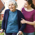 A carer assists an older lady to walk.