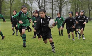 A boys holding a rugby ball being chased by other children playing rugby.