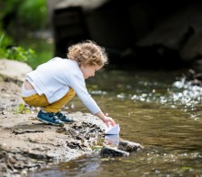 A toddler by a stream with a paper boat.