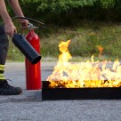 A fireman putting out a fire in a metal tray with an extinguisher.