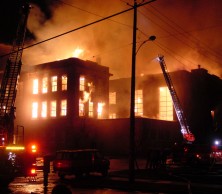 A large school burns at night whilst fire engines spray water.