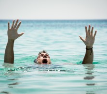 A man appears to be drowning, gasping for breath with hands reaching out of a body of water.