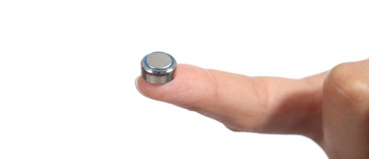 A person holding a button battery on a fingertip.