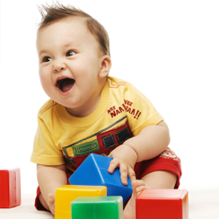 A happy baby clutches coloured blocks.