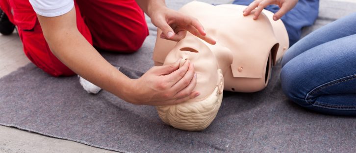 A medic in trousers teaching CPR on a dummy to a person in jeans.