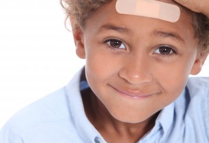 A little boy proudly shows off a plaster on his forehead.