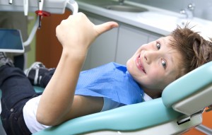 A male child in dentist chair giving thumbs up.