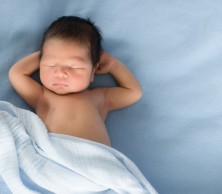 A peaceful sleeping baby with hands behind his head on blue blankets.