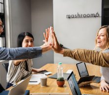 Supporting mental health in the workplace, a group of colleagues high five at a work desk.