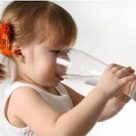 A young girl taking a sip of water from a glass.